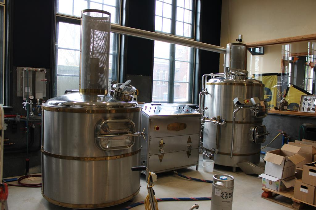 Tweee grote metalen brouwketels in een industriële ruimte met dozen op de voorgrond.