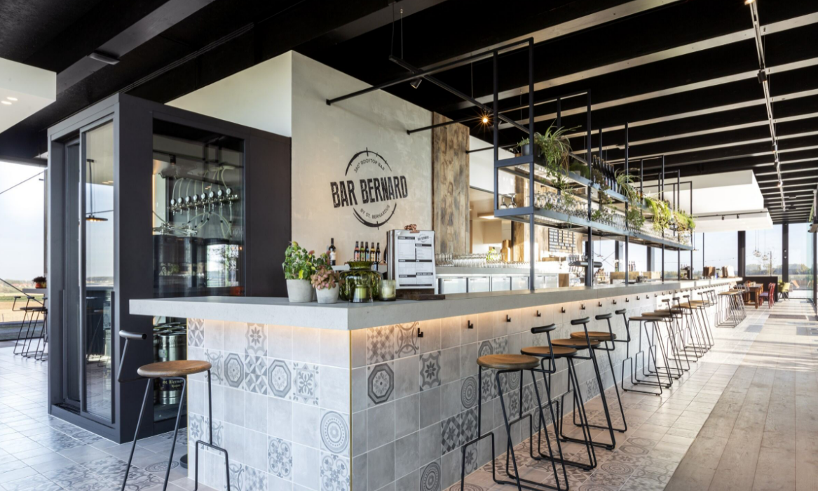 Modern ingerichte bar met hangende glazen en krukken bij de toog in Bar Bernard.