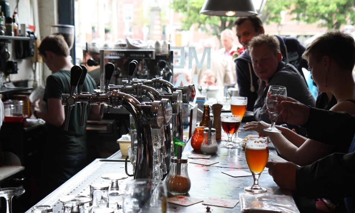 Mensen aan een bar genieten van bier met tappunten op de voorgrond.