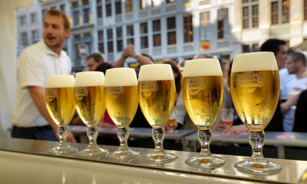 Rij glazen Stella Artois bier met schuimkraag op bar tijdens festival.