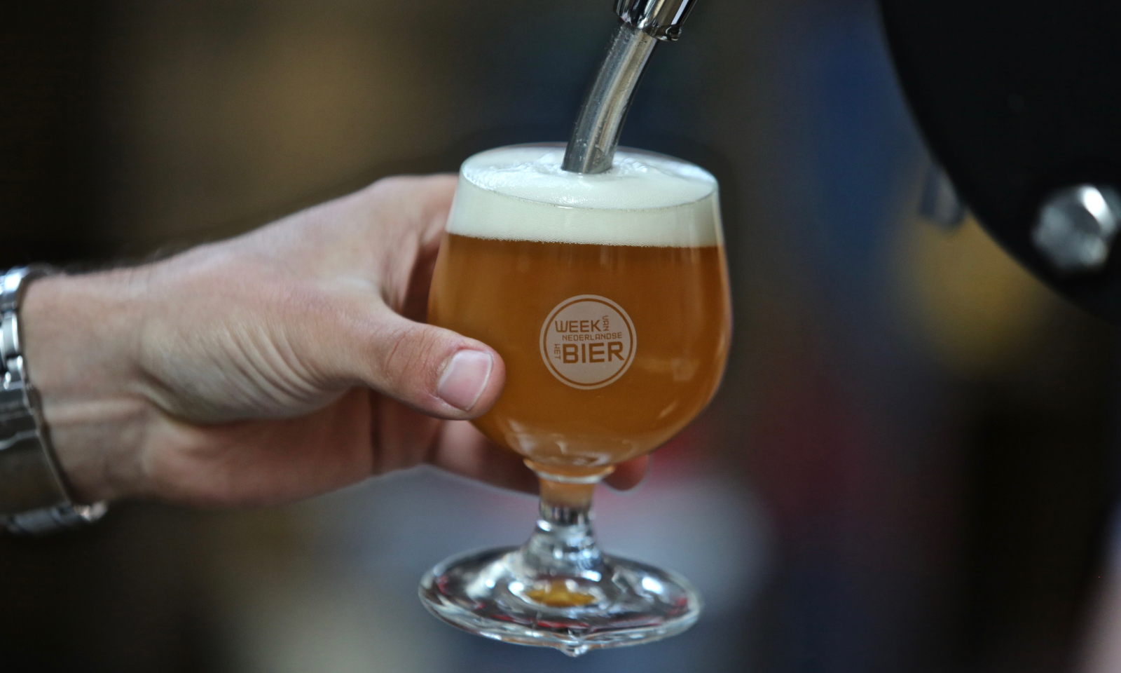 Hand houdt glas bier onder tap met opschrift 'Week van het Nederlandse Bier'.