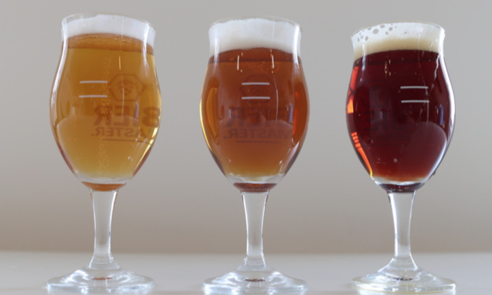 Drie glazen bier van verschillende kleuren op een witte achtergrond.