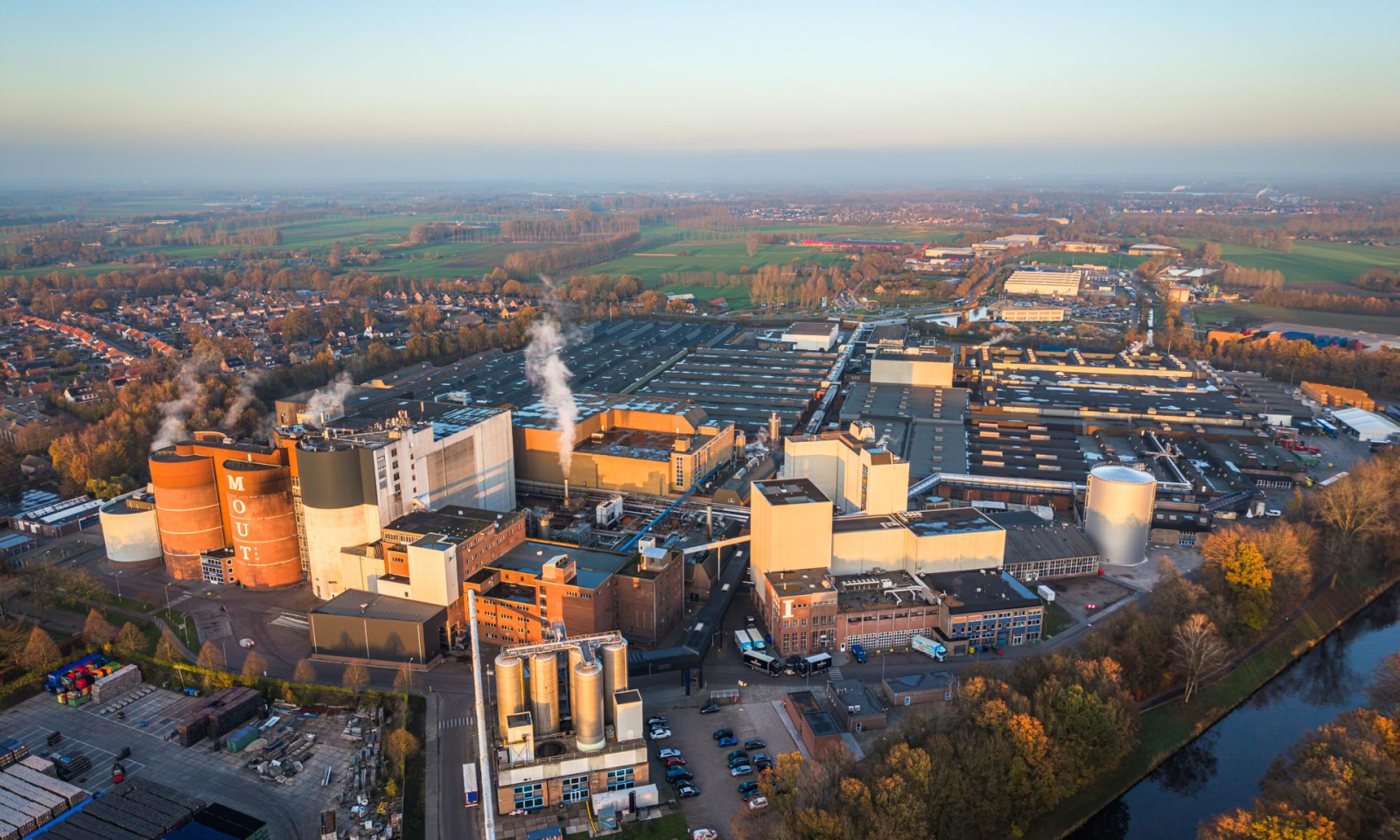 Luchtfoto van de Royal Swinkels brouwerij met stoom uit schoorstenen en omliggende natuur.
