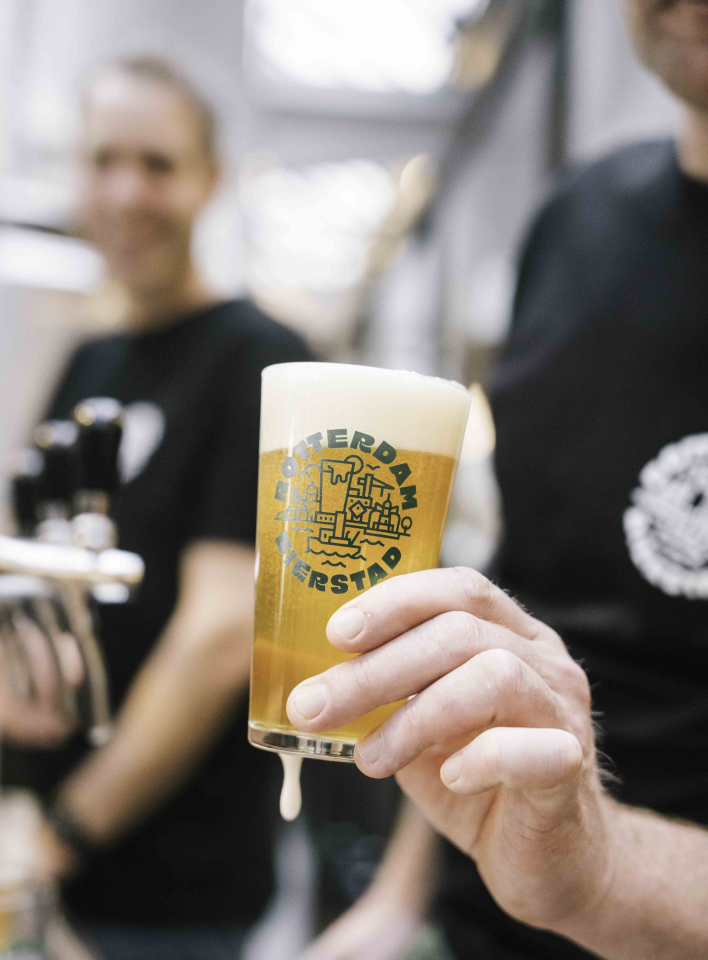 Hand houdt een glas bier vast met Rotterdam Bierfestival logo.