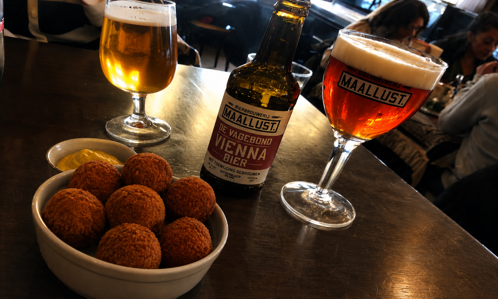 Bierglazen en een fles bier met schalen bitterballen op een tafel.
