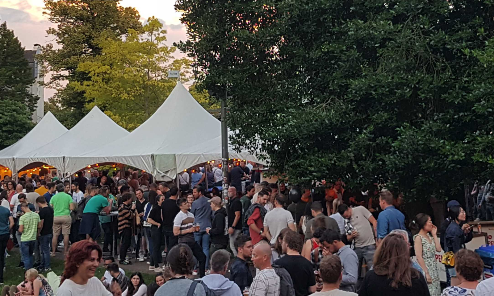 Groep mensen die buiten bijeenkomen bij witte tenten met feestverlichting.
