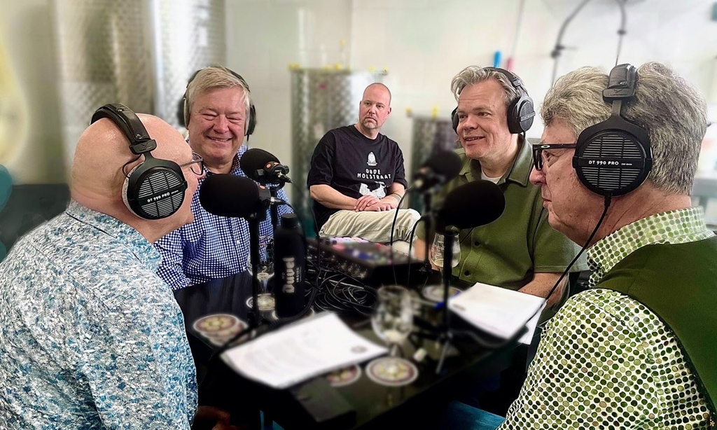 Vijf mannen met hoofdtelefoons in gesprek tijdens een podcastopname in een brouwerij.