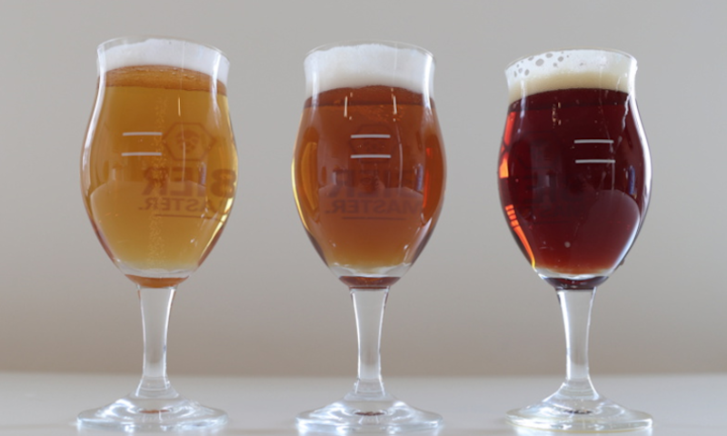 Drie glazen bier van verschillende kleuren op een witte achtergrond.