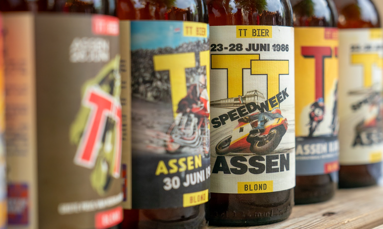 Flessen TT Bier met oude raceposters als etiketten, waaronder Assen 1986.
