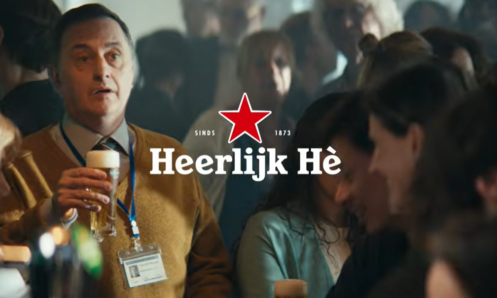 Man met bierglas en mensen op achtergrond bij Heineken campagne logo.