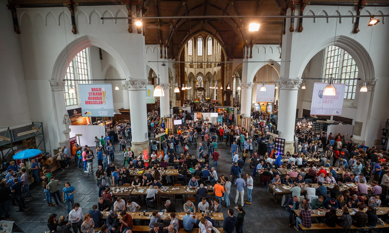 Binnenaanzicht van een druk bierfestival gehouden in een historische kerk met vele bezoekers.