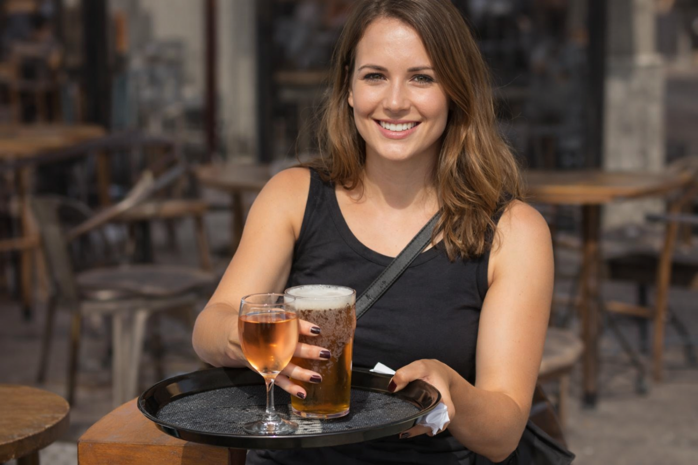 Vrouw houdt een dienblad met een glas wijn en een glas bier in een café.