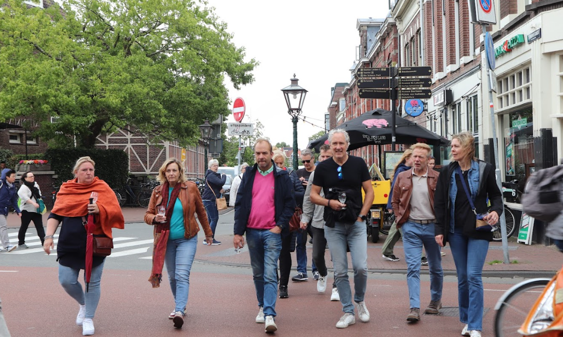Groep mensen wandelt over straat met gebouwen op de achtergrond.