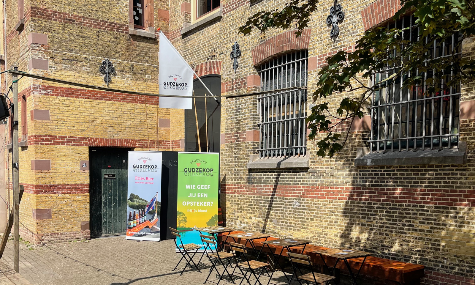 Terras met tafels en stoelen naast bakstenen muur met promotiemateriaal van Gudzekop.