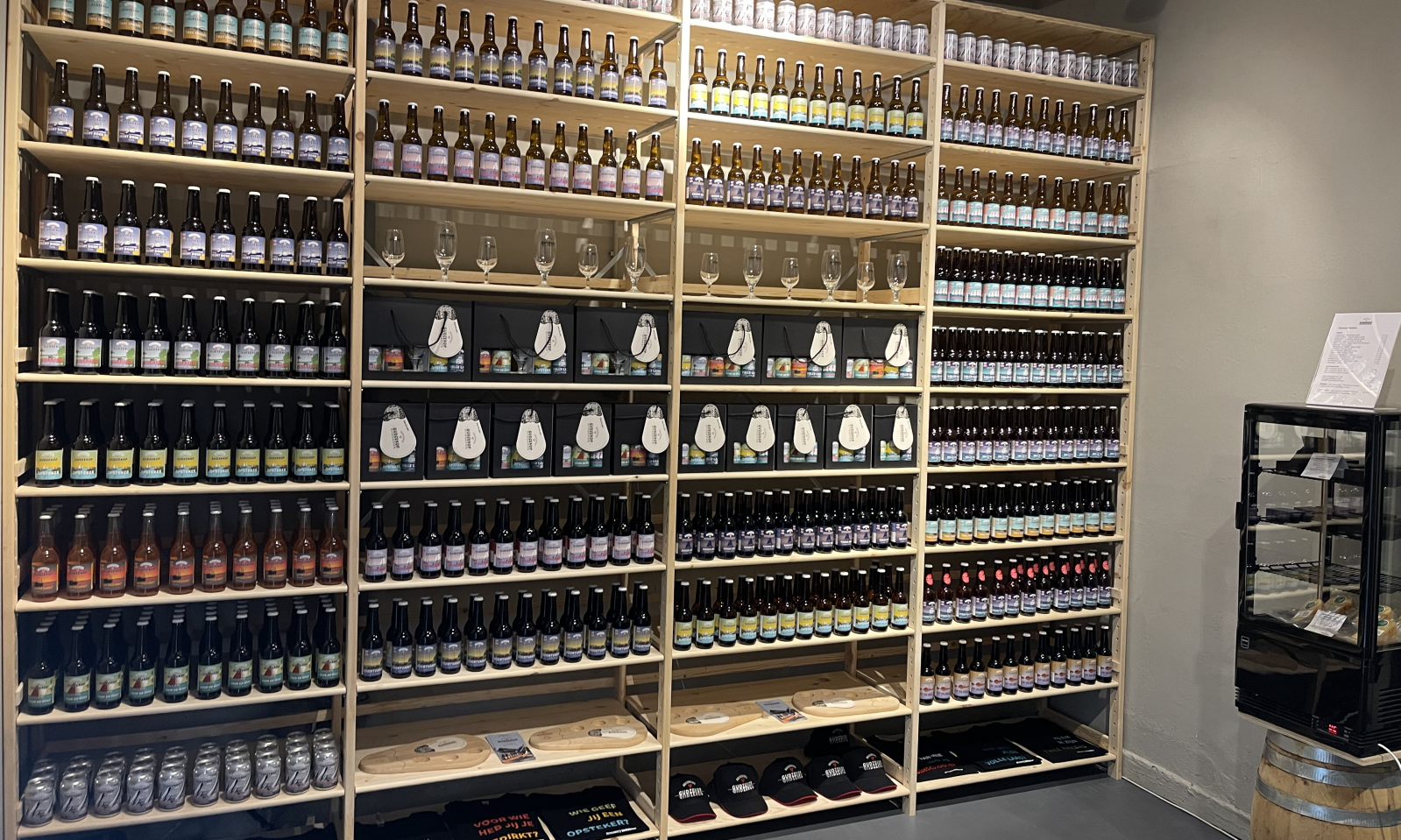 Muur met houten schappen vol verschillende flessen bier in een proeflokaal.