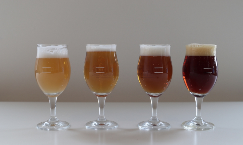 Vier glazen bier met variërende kleuren op een witte achtergrond.