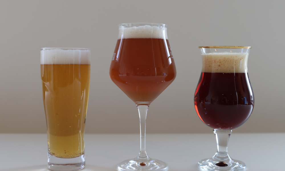 Drie glazen met verschillende kleuren bier op een witte ondergrond.