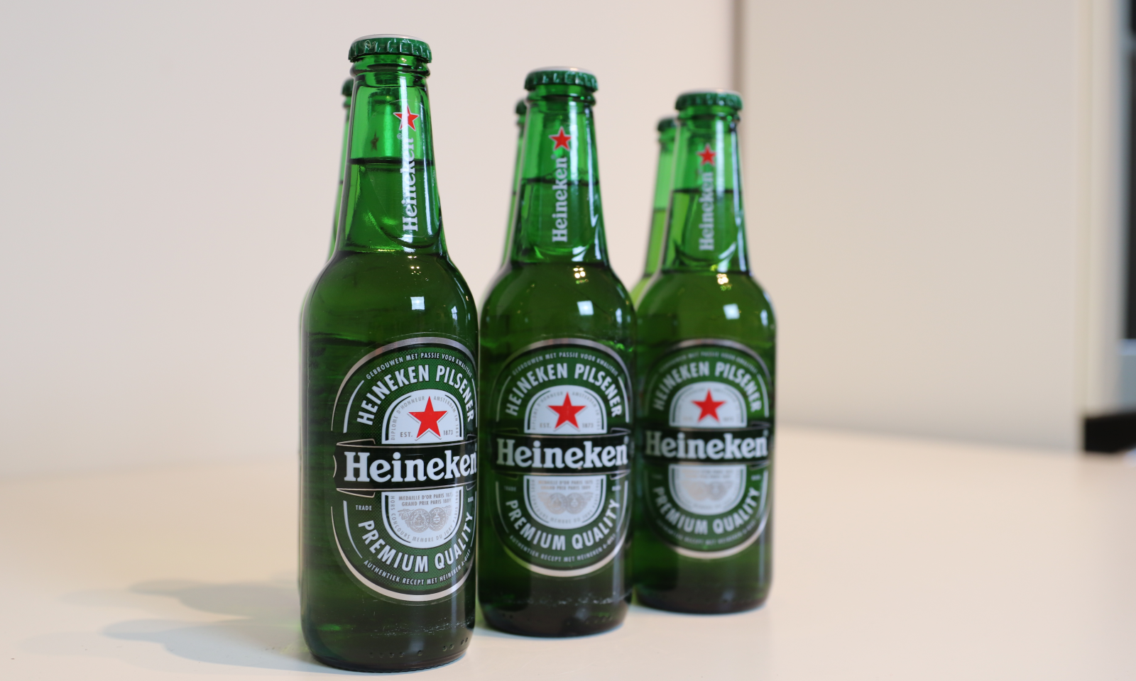 Vier groene Heineken bierflesjes op een witte tafel met een neutrale achtergrond.