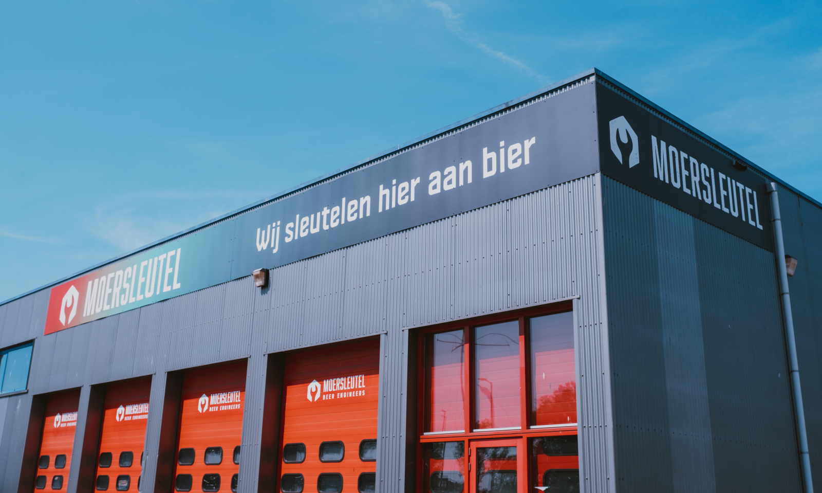 Buitenaanzicht van de Moersleutel bierbrouwerij met tekst 'Wij sleutelen hier aan bier'.