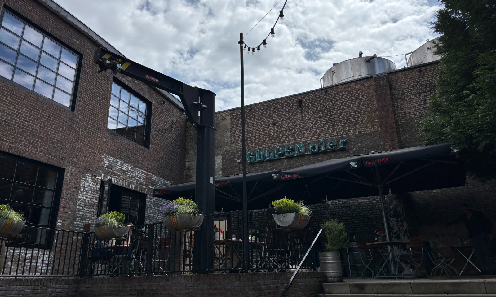Terras bij een bakstenen brouwerijgebouw met Gulpener-parasols en het bord Gulpener bier.