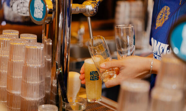 Bier wordt aan de tap geschonken in een glas met Homeland-logo tussen gestapelde glazen.