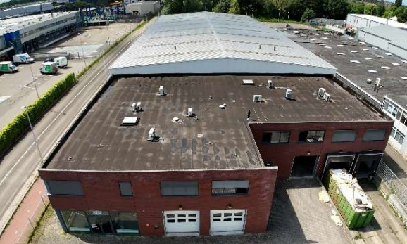 Dronebeeld van een rood bakstenen bedrijfspand met platte daken in een industriegebied.