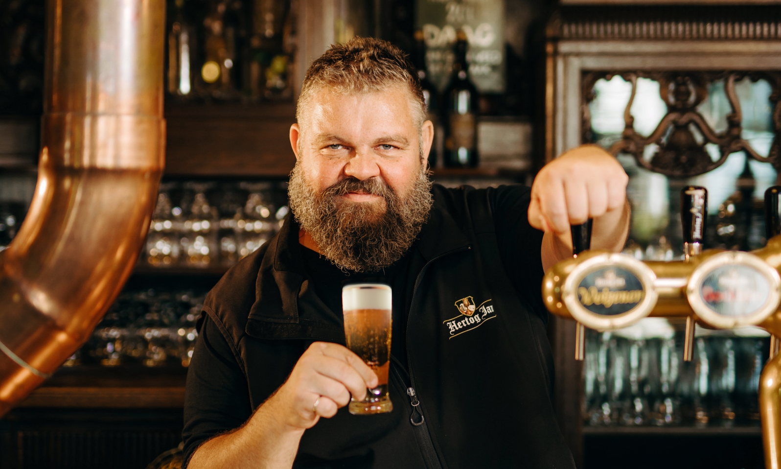 Meesterbrouwer Micha Peute van Hertog Jan achter de bar met een glas pils in de hand