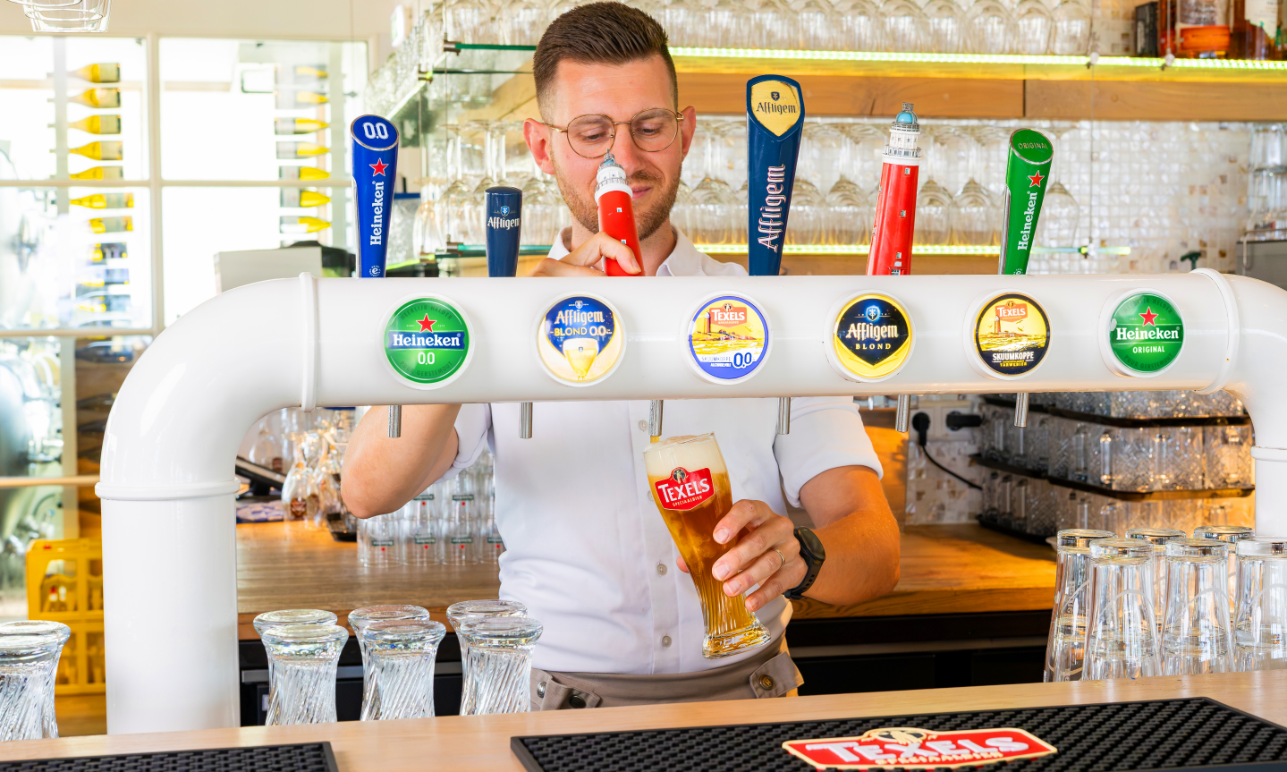 Barman tapt Texels bier achter een witte tap met onder meer Texels Skuumkoppe 0.0.