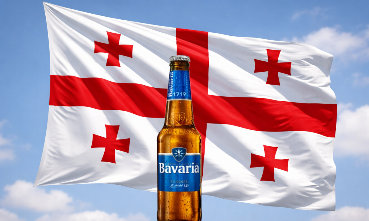 Bavaria-bierfles voor een wapperende Georgische vlag tegen een blauwe lucht.