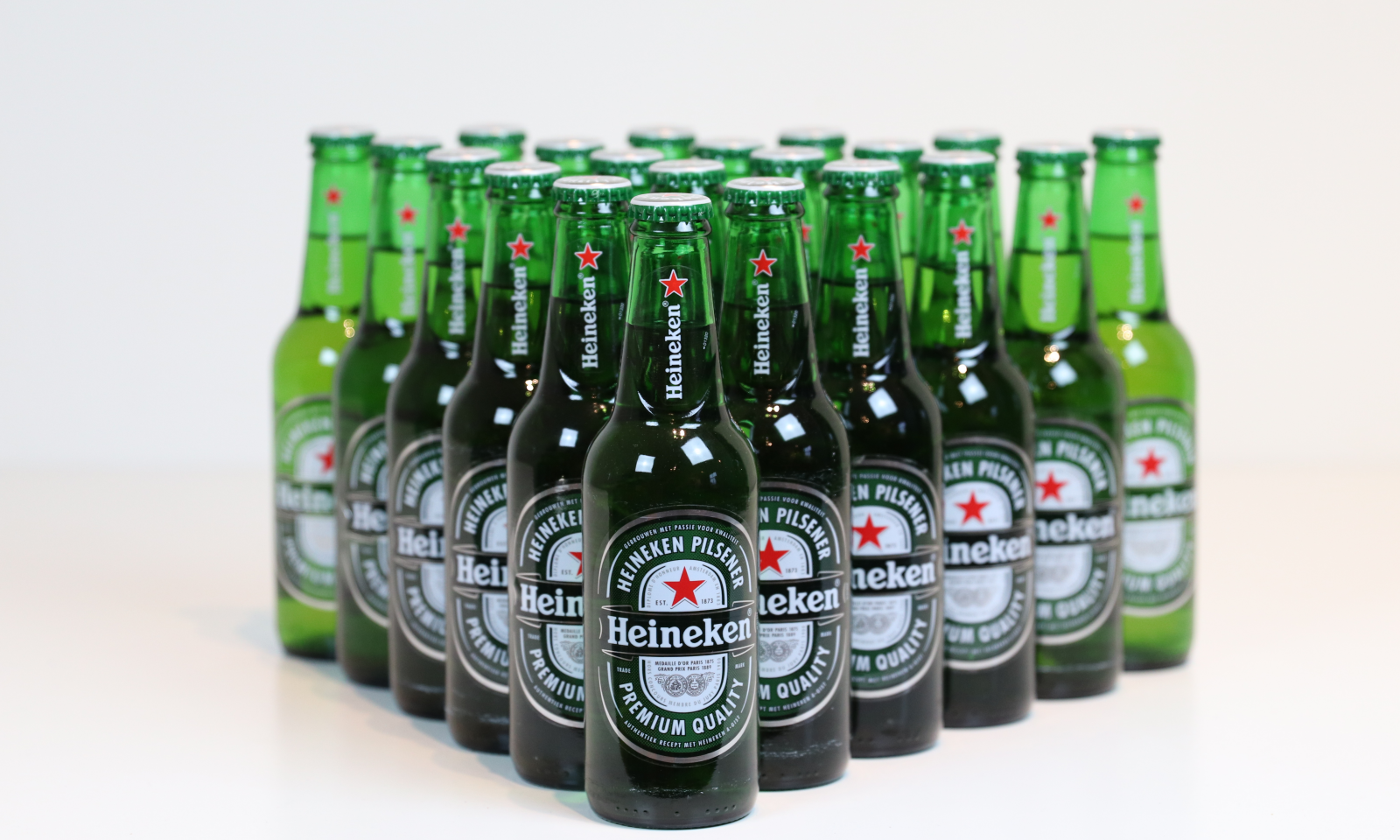 Groep groene Heineken-bierflesjes in rijen tegen een lichte achtergrond.