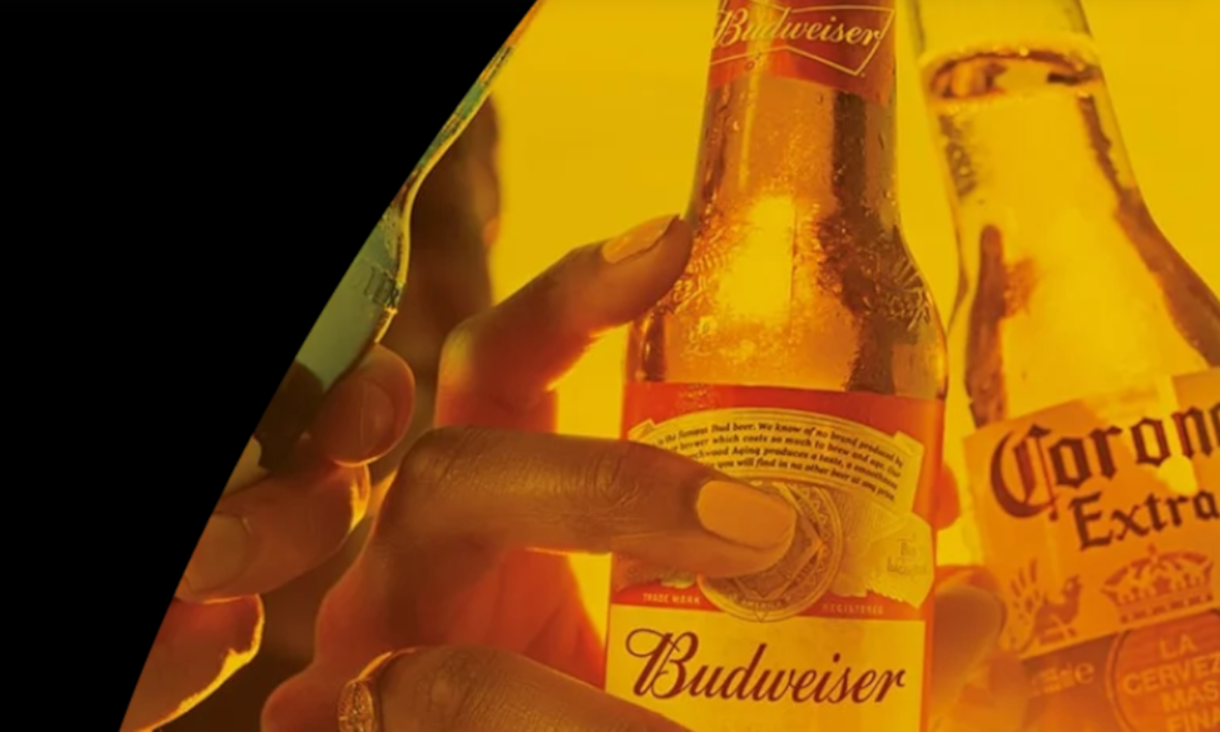 Close-up van handen met Budweiser- en Corona-bierflessen tegen een warme gele achtergrond
