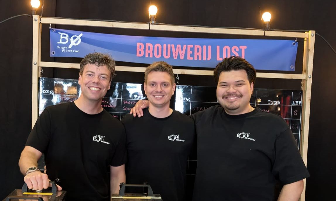 Stan, Lorenzo en Michiel in zwarte shirts voor een stand van Brouwerij Lost met blauwe banner.