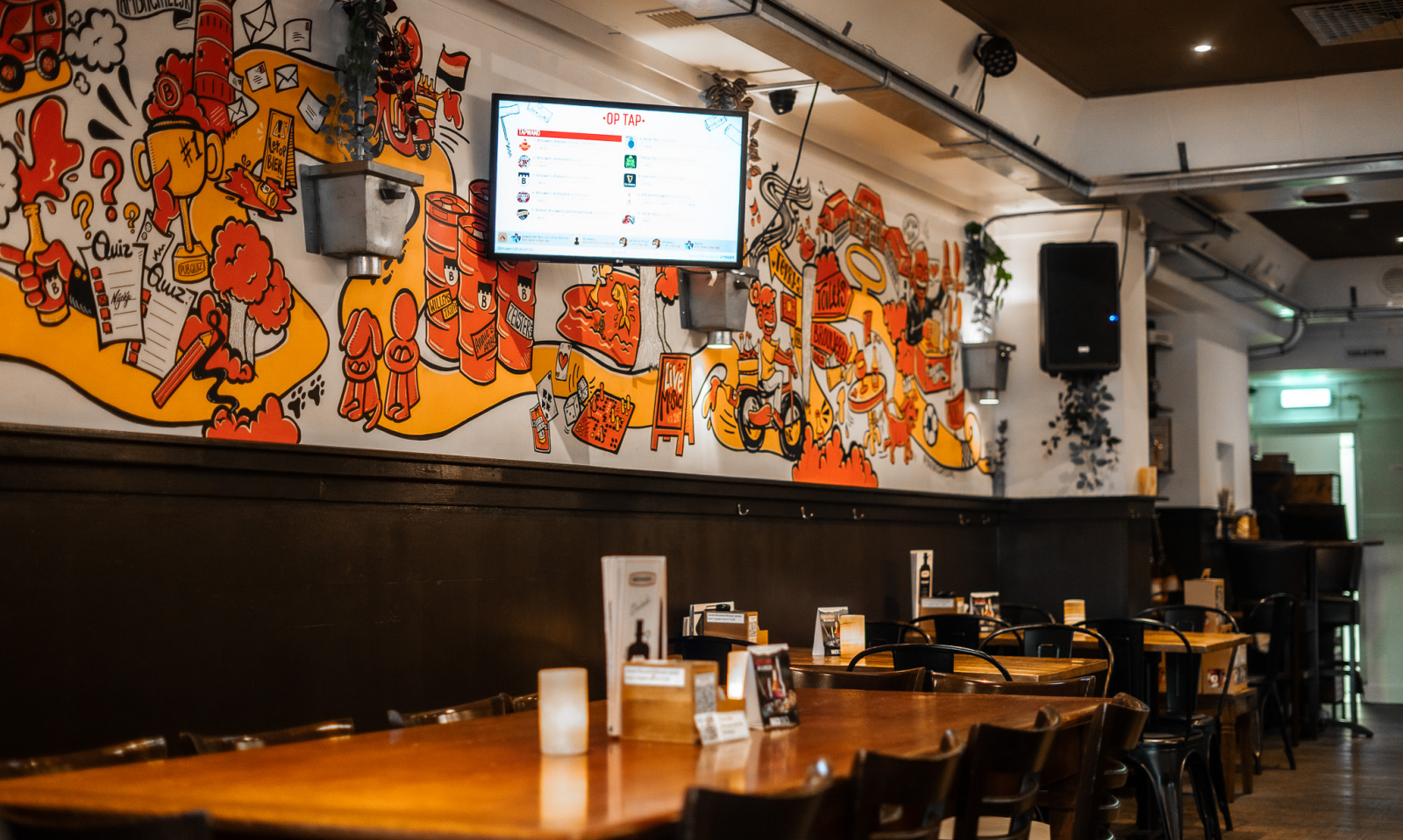 Café-interieur van Brouwerij Brasser met houten tafels, donkere lambrisering en kleurrijke muurschildering aan de wand.