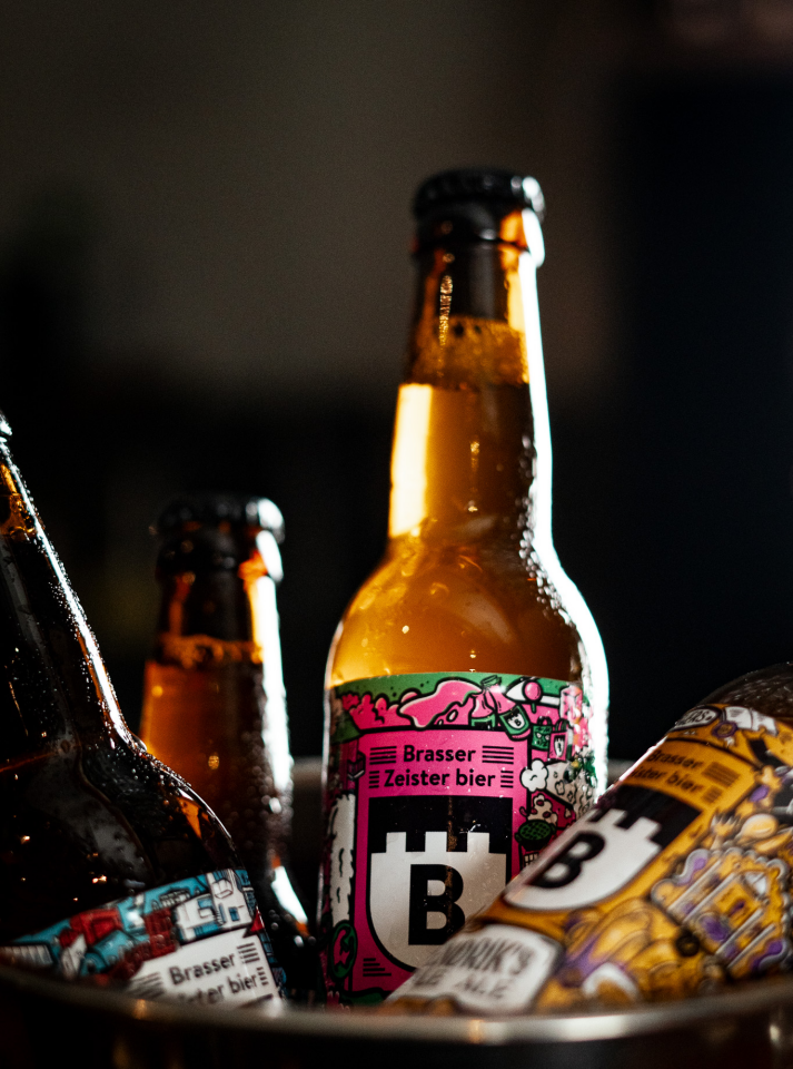 Close-up van amberkleurige bierflessen met centraal een Brasser Zeister bier-fles met kleurrijk etiket.