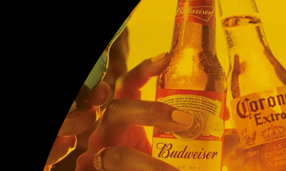 Handen houden een Budweiser-bierfles vast tegen een warme gele achtergrond.