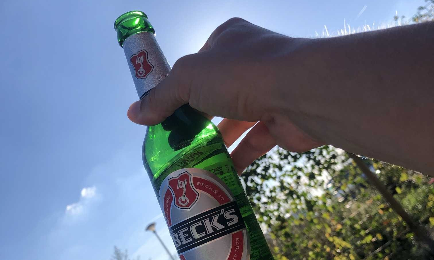 Diederik van Biernet.nl houdt een groen flesje Beck's bier omhoog tegen een zonnige blauwe lucht.