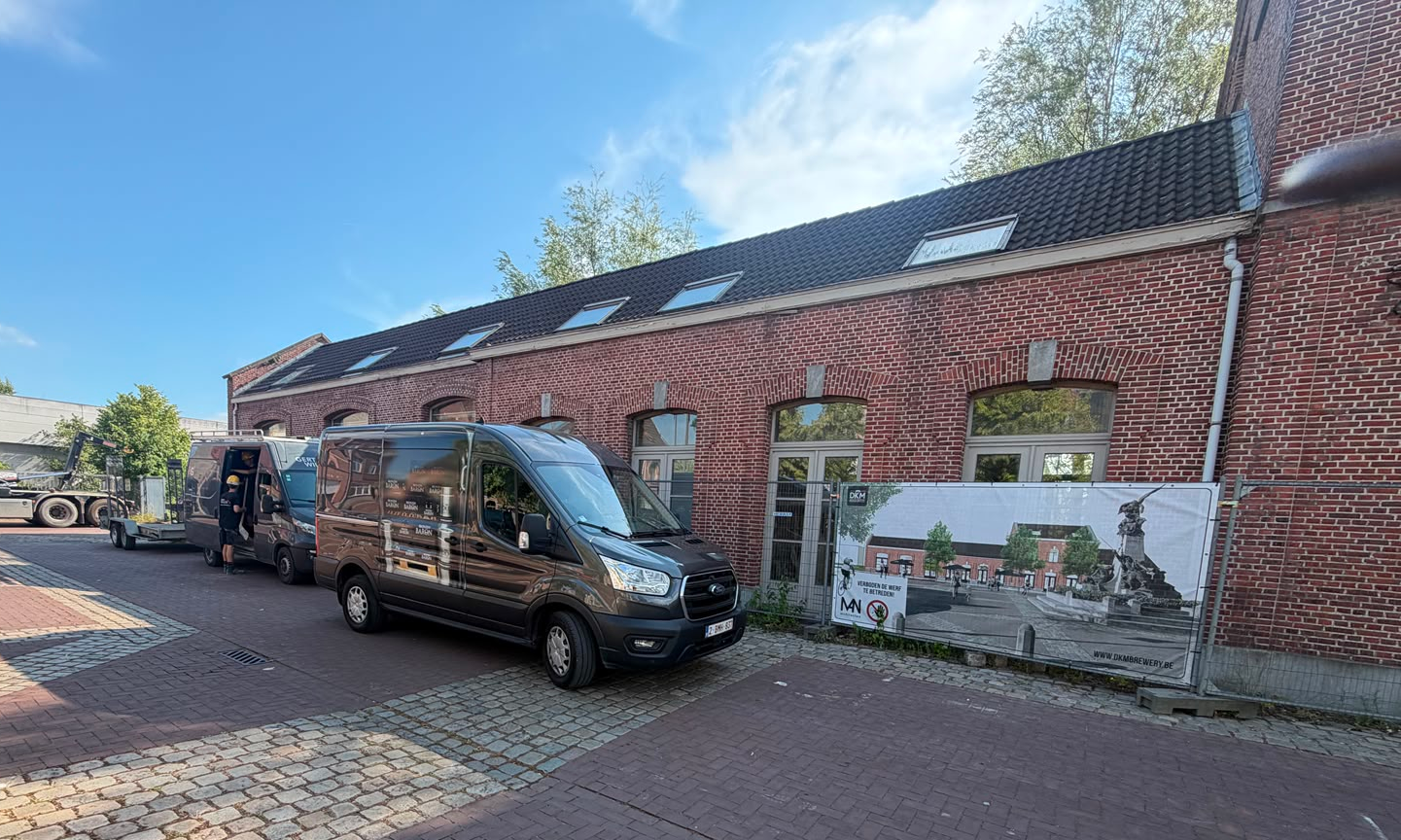 Zwarte bestelwagens voor een rood bakstenen pand met DKM Brewery-bouwbanner in Hamme.