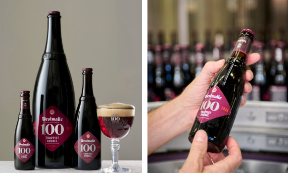 Westmalle 100 Trappist Dubbel flessen en glas naast een hand die een jubileumfles vasthoudt.