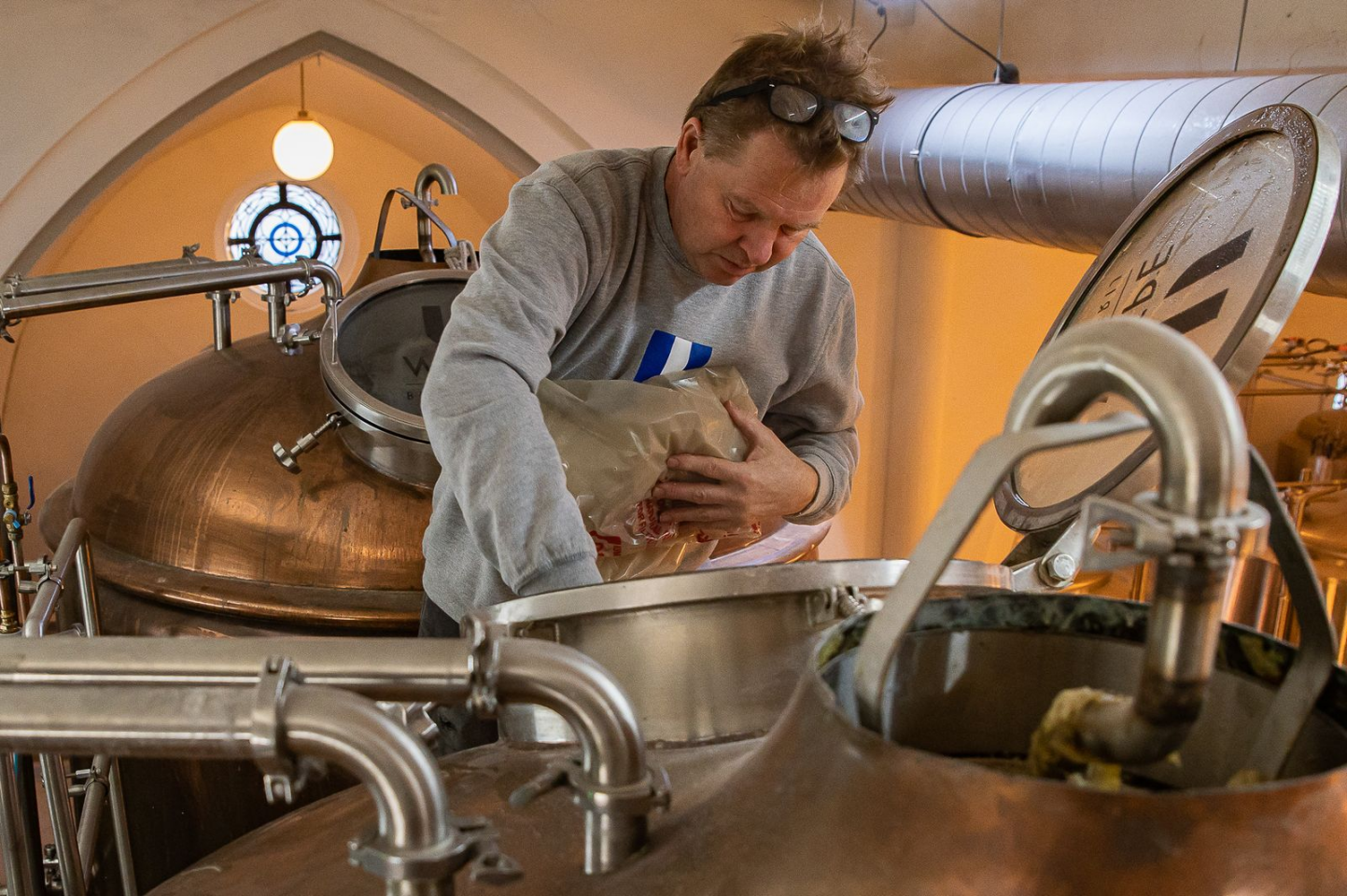 Brouwer voegt mout toe aan een koperen brouwketel in een ambachtelijke brouwerij.