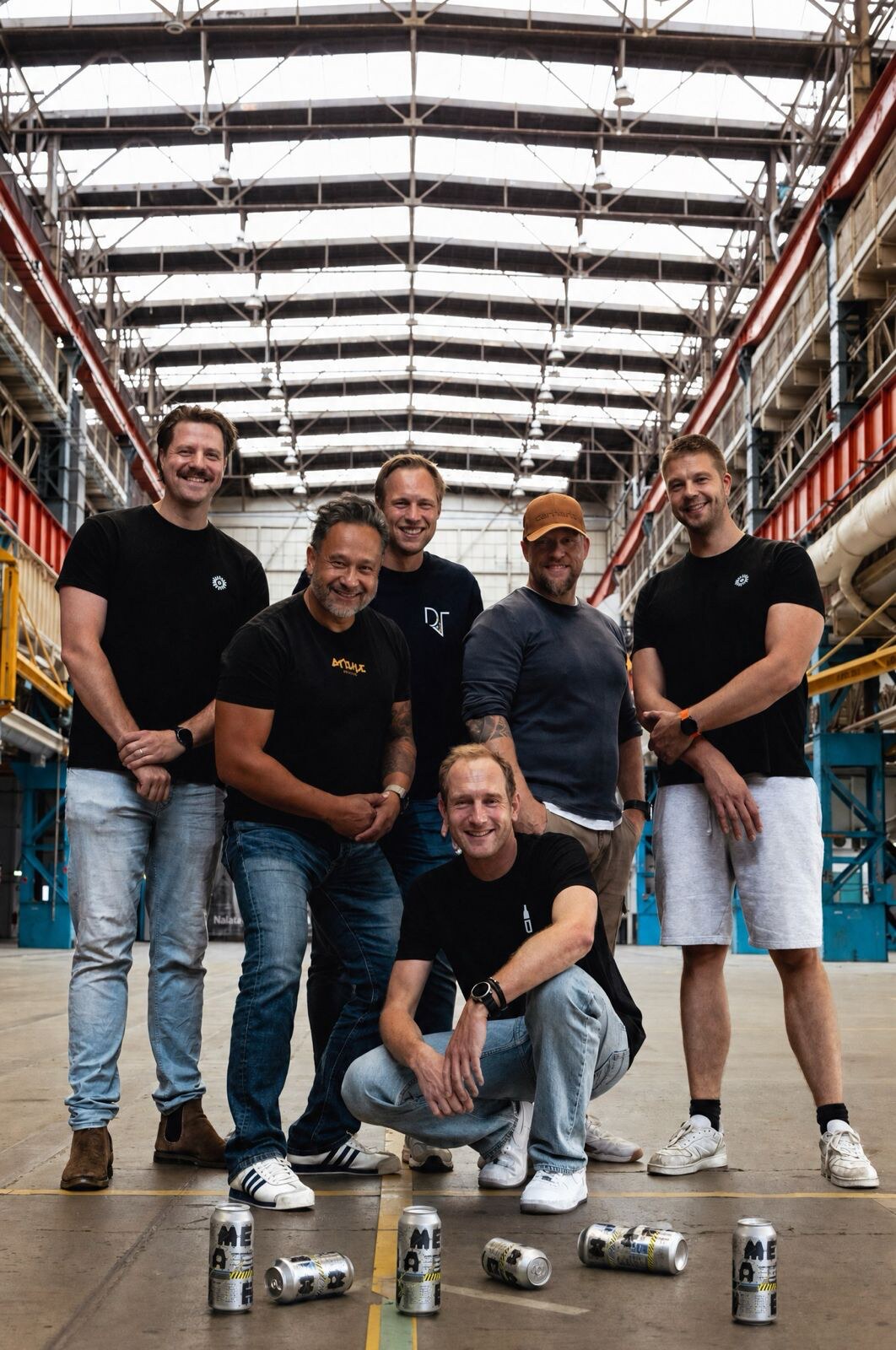 Zes makers van het bier METAALWERK in de oude machinehal van Stork in Hengelo, met blikken van het bier op de vloer.