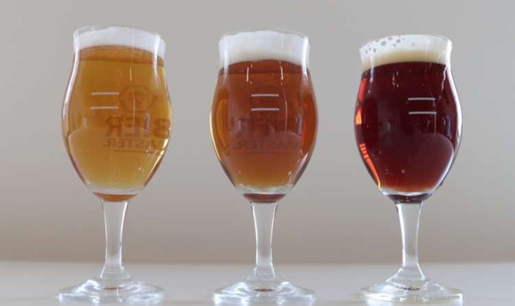 Drie proefglazen met verschillende soorten bier en schuimkraag op een lichte tafel.