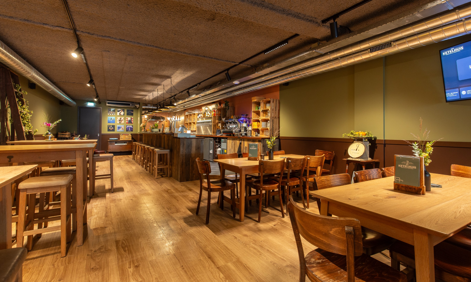 Warm interieur van biercafé ZWOL met houten tafels, bar, tapkranen en industriële plafondbuizen.