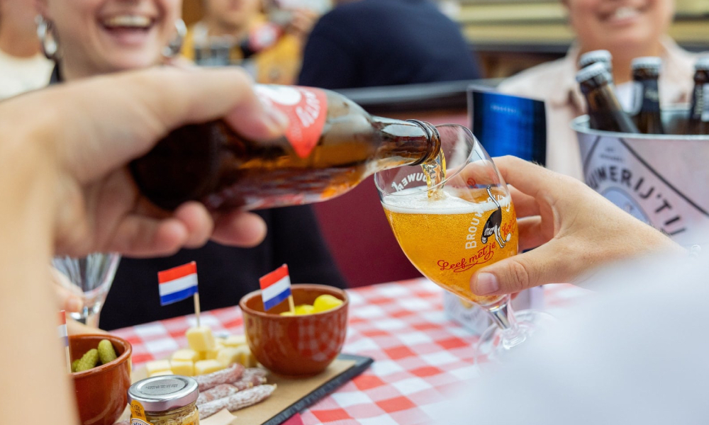 Bier wordt ingeschonken in een Brouwerij ’t IJ-glas naast borrelhapjes en Nederlandse vlaggetjes.
