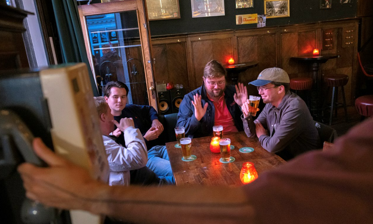 Jonge mannen drinken bier aan een houten tafel in een sfeervol bruin café met kaarslicht.