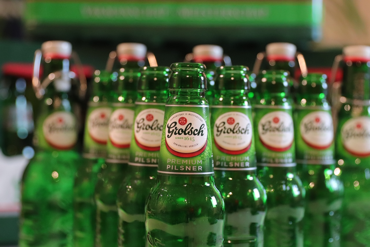 Rij groene bierflesjes met labels en kroonkurken, centraal één scherp flesje.