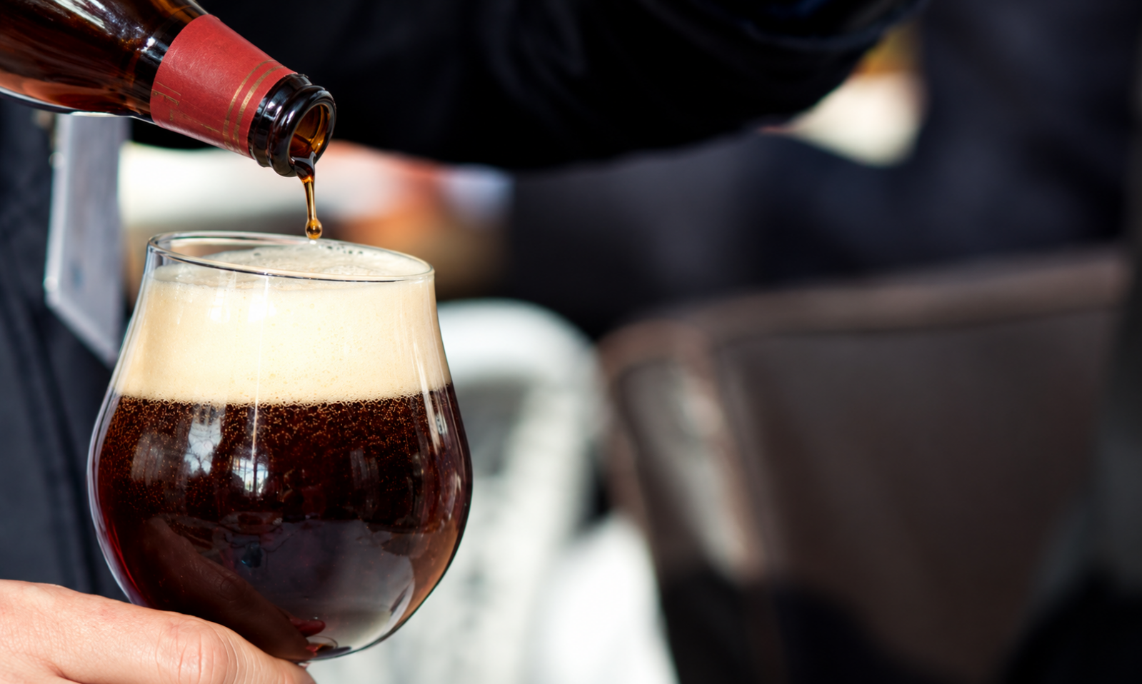 Donkere bierglas met schuim terwijl bier uit een fles wordt ingeschonken