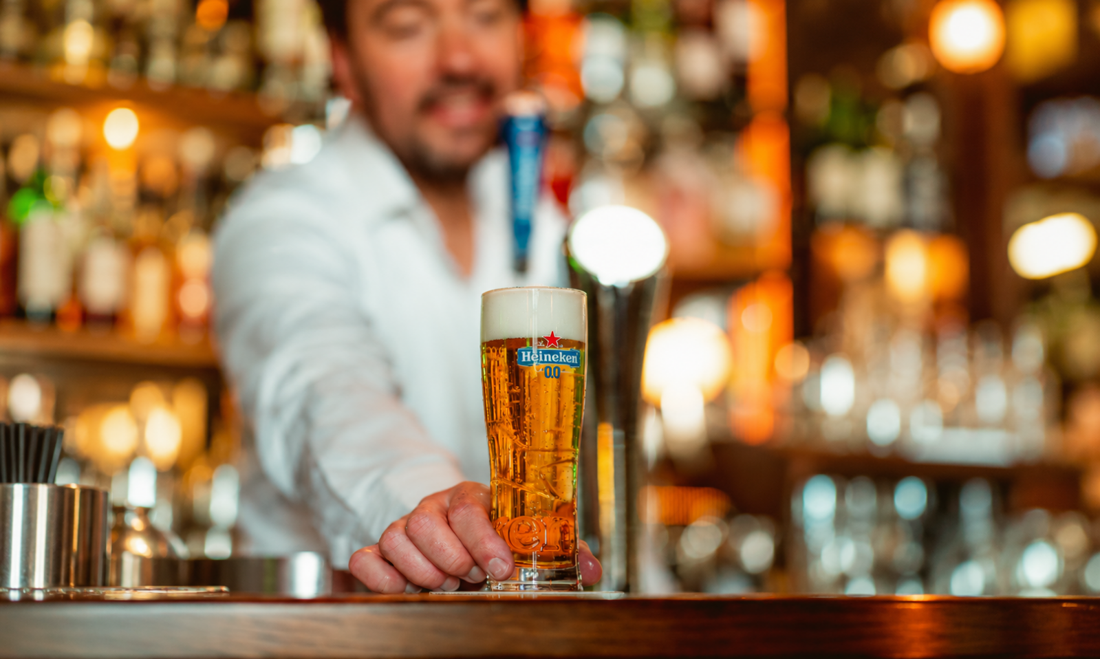 Glas met alcoholvrij Heineken bier op een bar met barman op de achtergrond