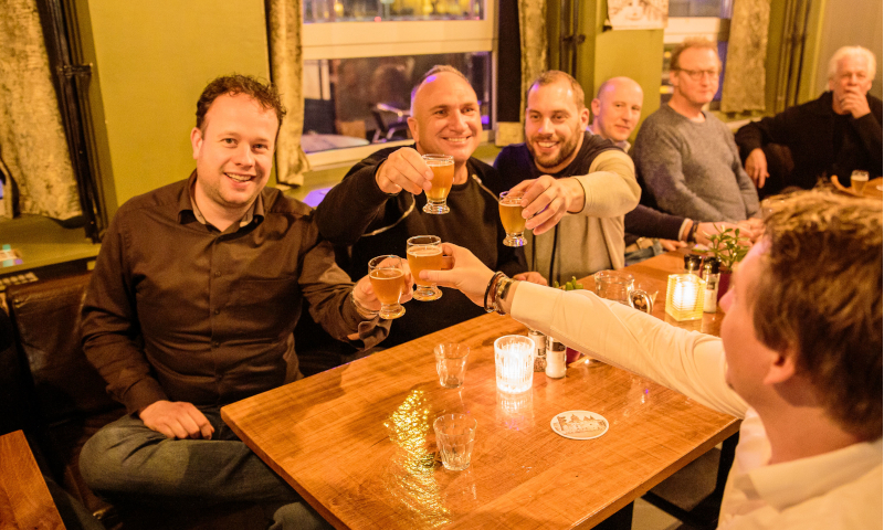 Mannen aan tafel die proosten met bier