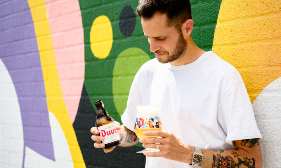 Duvel Designer bierglas 2023 en een flesje Duvel vastgehouden door Hedof