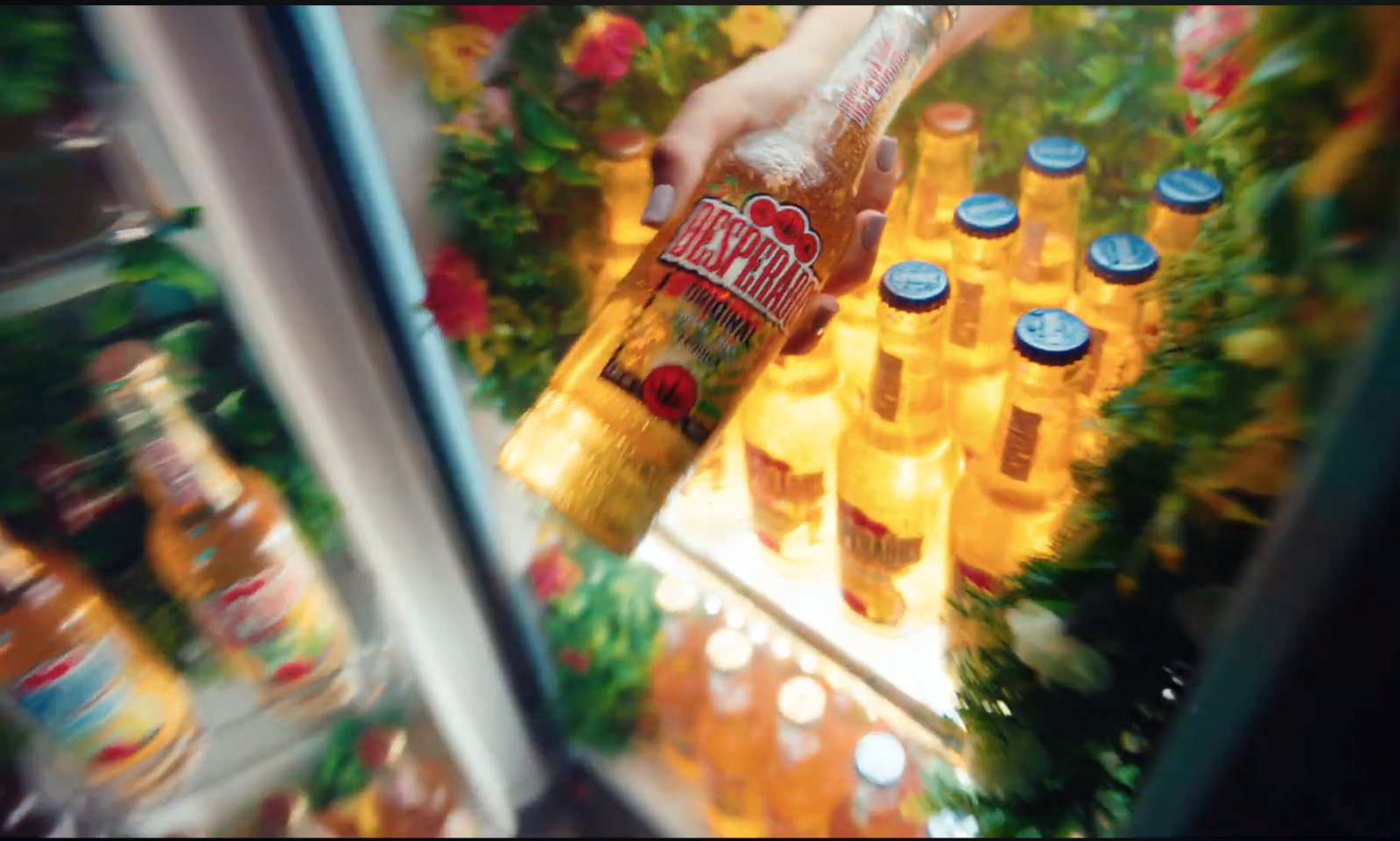 Hand pakt Desperados fles uit kleurrijke koelkast met bloemen en flesjes.